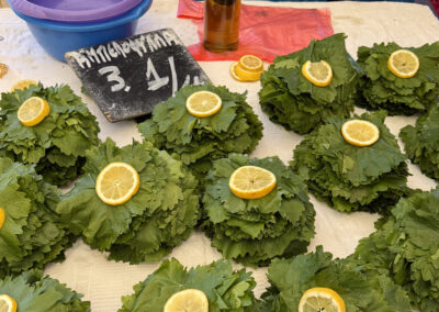 Pile of large green leaves with lemon halves arranged on a table; a bottle sits in the center and a chalkboard sign is nearby.