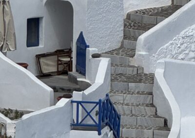 Whitewashed stairs and blue railing wind up a Greek island house with curved walls and blue door(s).