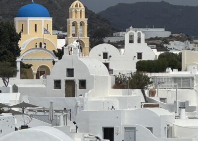 Whitewashed Cycladic buildings with a bright blue-domed church and bell tower against a rocky hillside on a Greek island.
