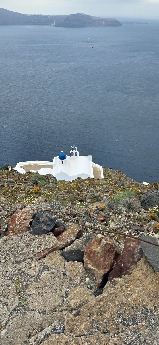 Resized1756381543734 Theoskepasti church CC - Taussig Travel White-washed church with a blue dome perched on a rocky cliff overlooking the deep blue sea below.