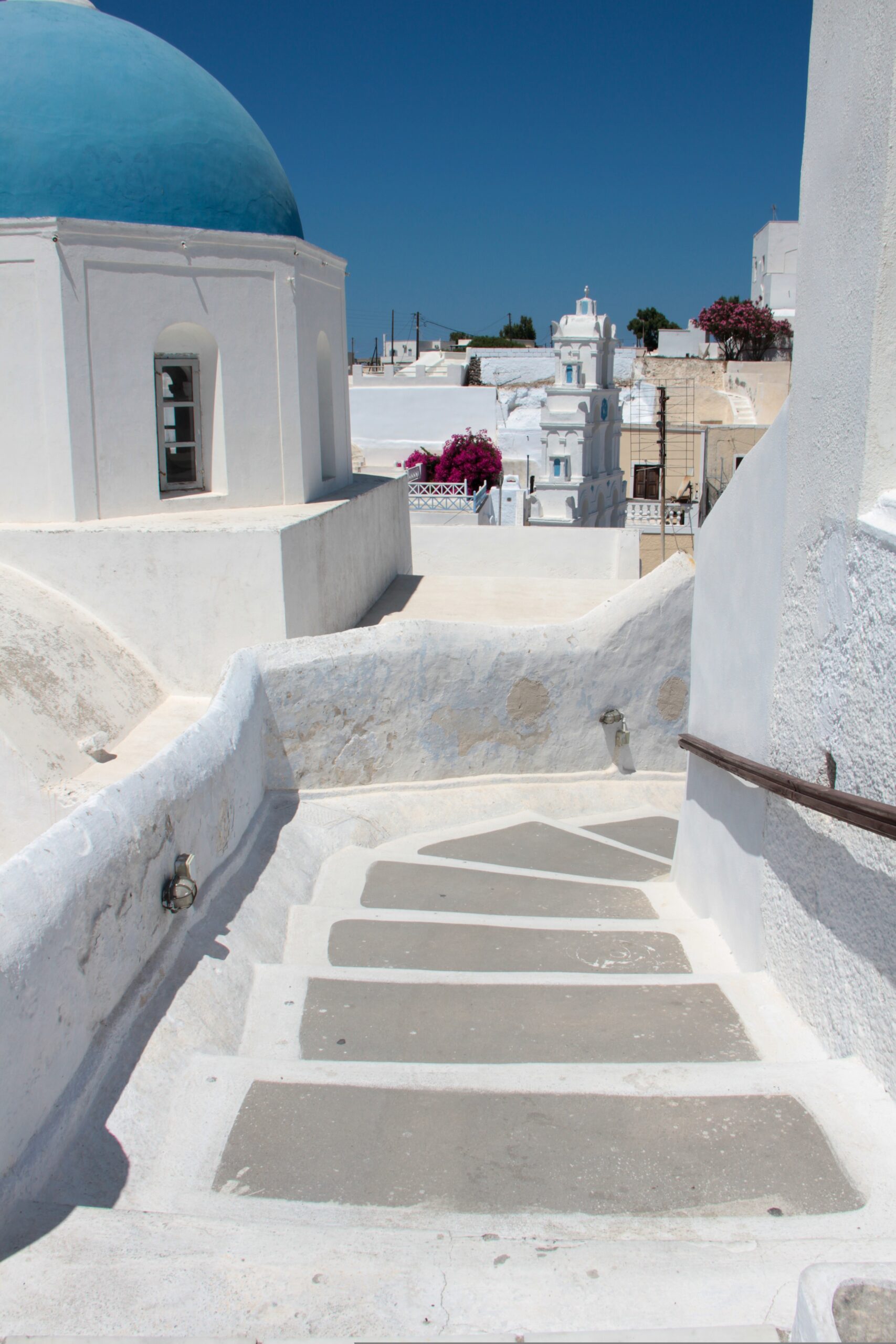 pat_photographies-megalochori-4382244 - Taussig Travel White-washed buildings with a blue-domed roof, steps, and a bright blue sky in a Greek island scene.