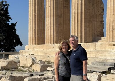 Couple posing in front of tall ancient limestone columns at a historic site, blue sky behind them.